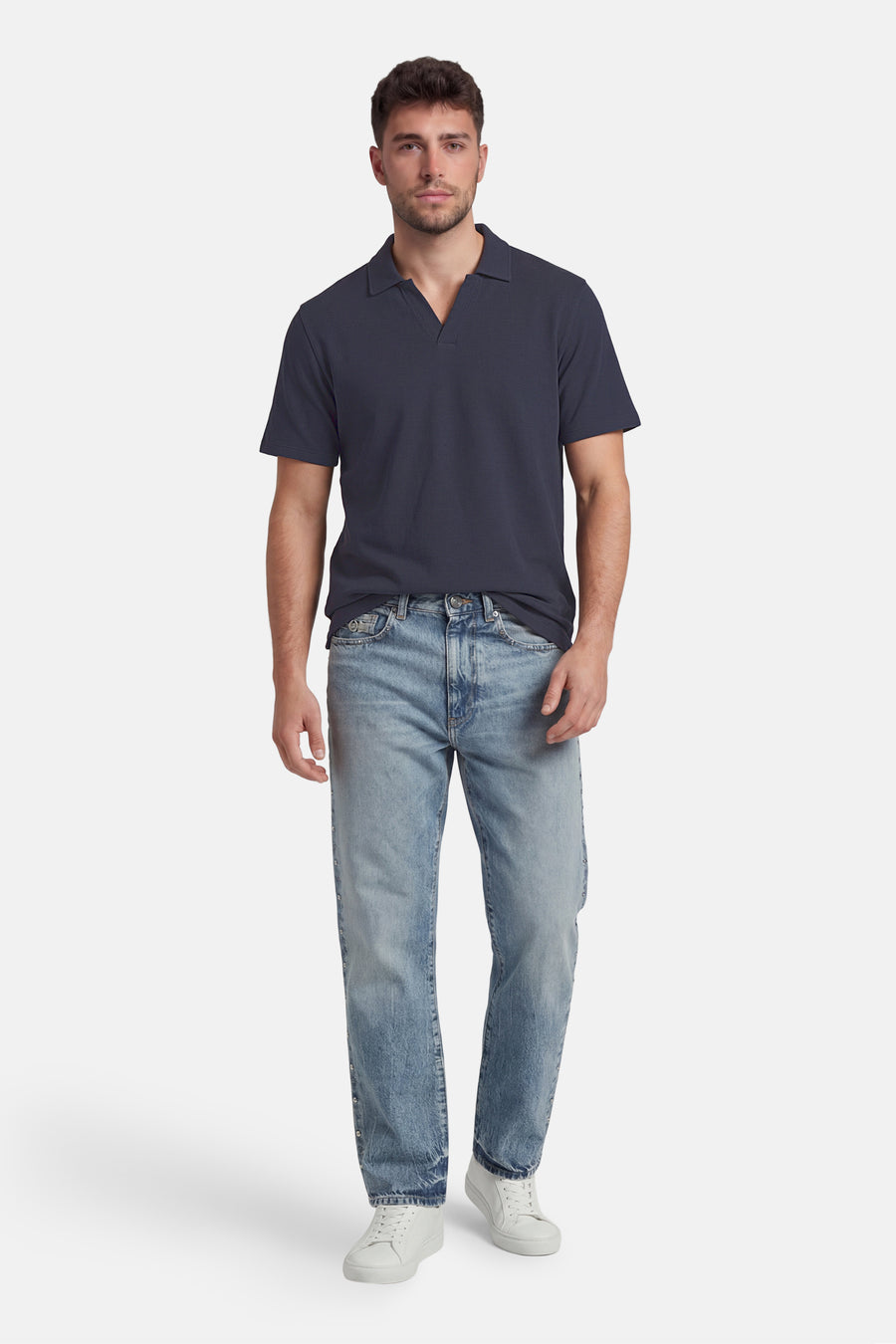 Polo bleue de ORIGINALS BY JACK & JONES avec col ouvert, portée par un homme en jean bleu clair avec des clous et des baskets blanches.