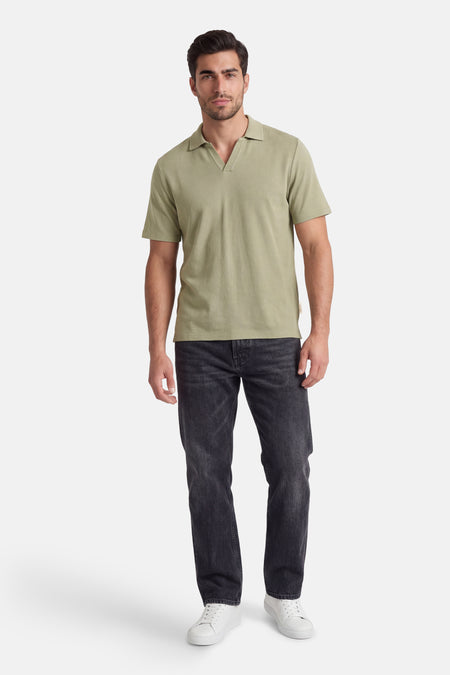 Polo verte ORIGINALS BY JACK & JONES, avec col en V ouvert, portée par un homme avec un jean noir et des baskets blanches.