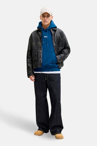 Sweat à capuche bleu de CORE BY JACK & JONES, avec veste en cuir foncé, jean ample et bottes beiges.