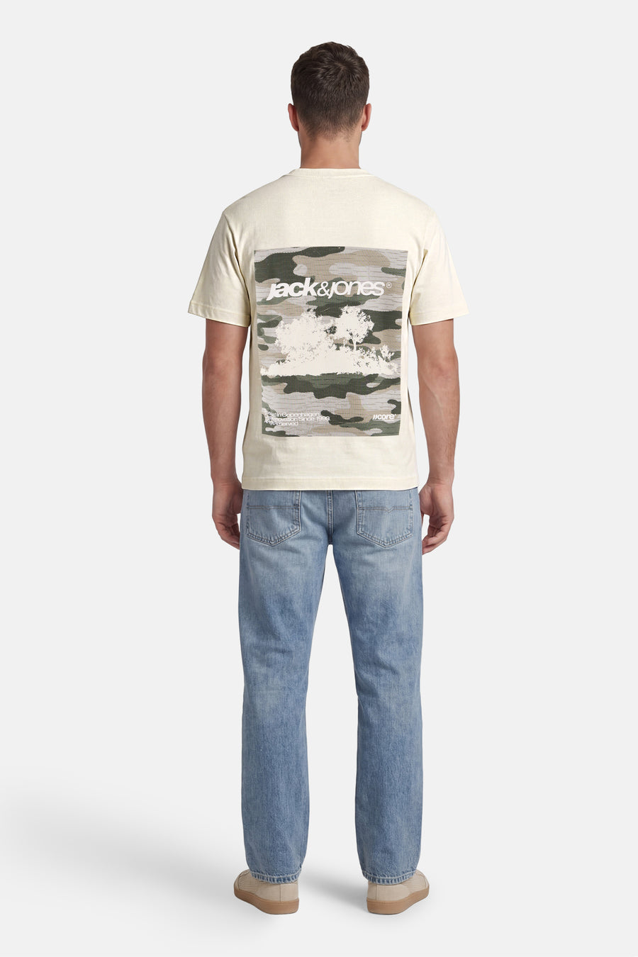 T-shirt écru de CORE BY JACK & JONES avec imprimé camouflage et logo blanc dans le dos, porté par un homme avec un jean bleu et des chaussures beiges (vue de dos).