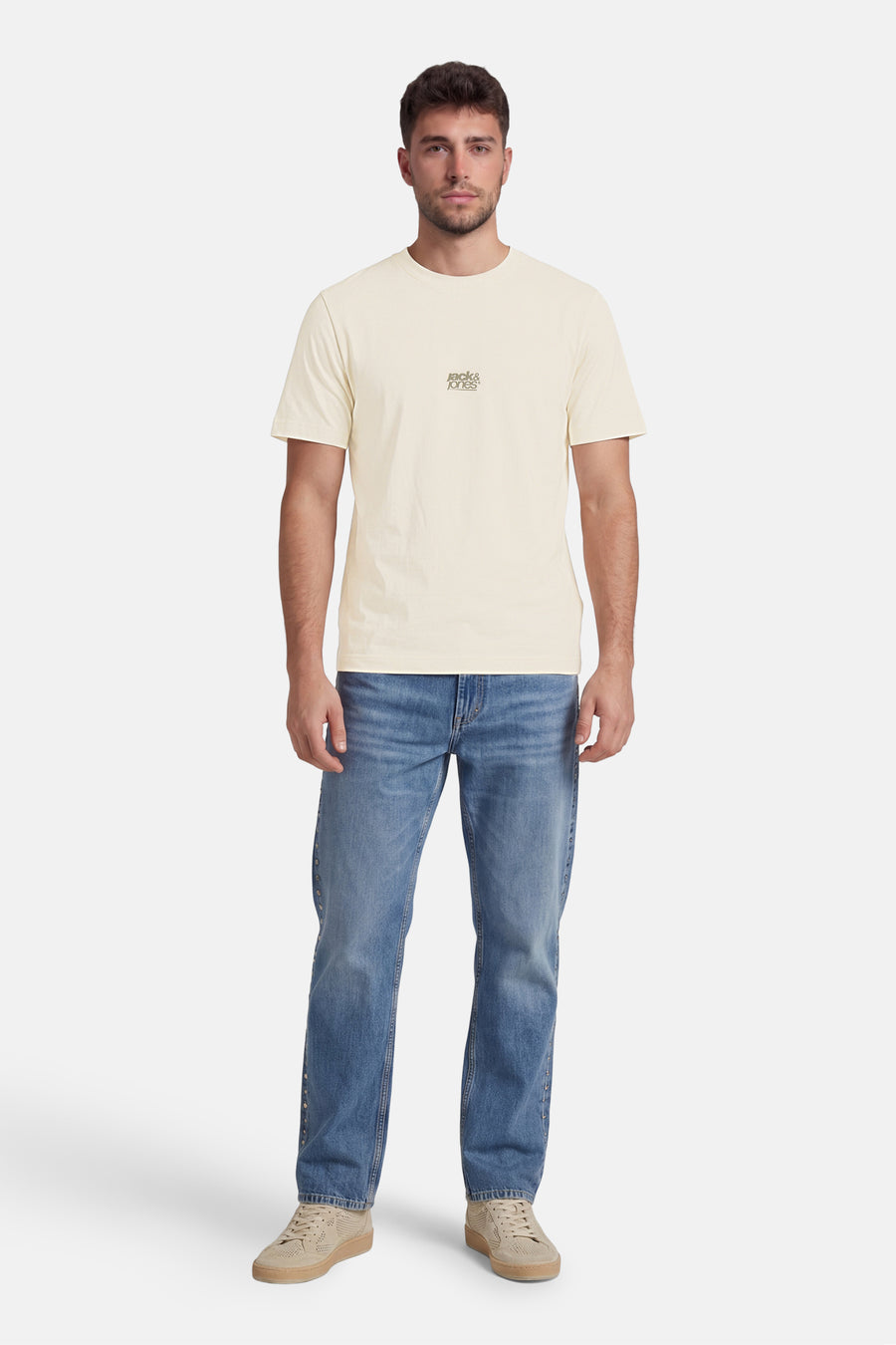 T-shirt écru de CORE BY JACK & JONES avec petit logo sur la poitrine, porté par un homme avec un jean bleu et des baskets beiges.