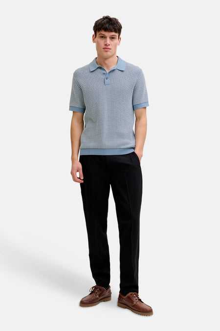Blauwe polo van PREMIUM by JACK & JONES, met een subtiel gemêleerd patroon, gecombineerd met zwarte pantalon en bruine schoenen.
