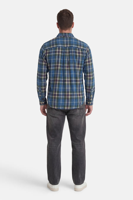 Chemise à carreaux bleus à manches longues de JACK & JONES, portée par un homme avec un jean foncé et des baskets blanches, vue de dos.