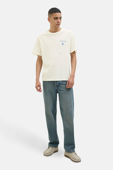 Wit T-shirt met korte mouwen van ORIGINALS BY JACK & JONES, met blauwe "Mykonos" tekst en een blauw oog. De man draagt blauwe jeans en beige instappers.