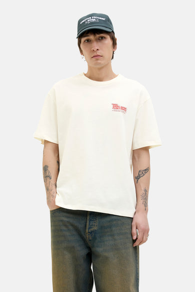 T-shirt blanc à manches courtes d'ORIGINALS BY JACK & JONES, avec une impression de texte rouge, associé à des jeans foncés et un casque.