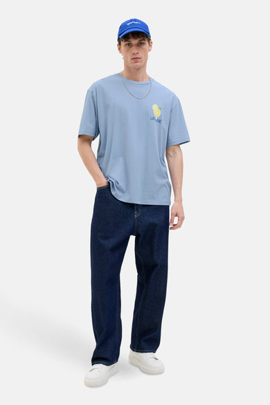 T-shirt bleu à manches courtes d'Originals by Jack & Jones, avec un design de citron, porté avec des jeans foncés et des baskets blanches.