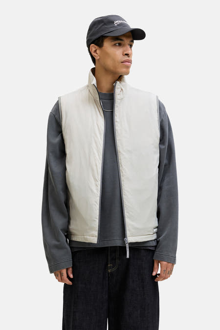 Gilet gris de CORE BY JACK & JONES, avec un t-shirt gris à manches longues, un jean foncé et une casquette grise.