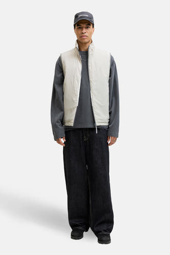 Grijze bodywarmer van CORE BY JACK & JONES, met lange mouwen grijs shirt, donkere jeans en grijze pet.