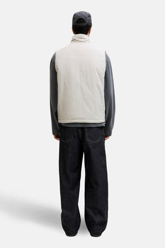 Gilet gris de CORE BY JACK & JONES, avec col montant et porté sur un t-shirt gris et un jean ample bleu foncé.