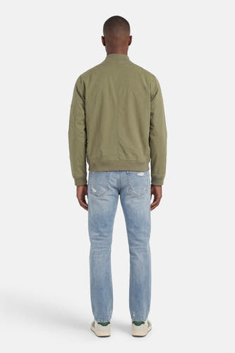 Veste courte verte de CORE BY JACK & JONES, vue de dos, avec texture tissée, poignets côtelés et poche sur la manche, portée avec un jean bleu clair et des baskets.