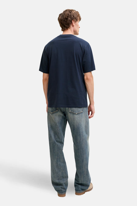 Achterkant van een man met blauw T-shirt en spijkerbroek.