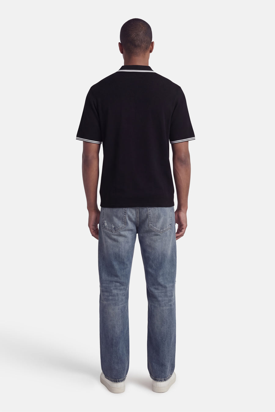 Zwarte polo met korte mouwen van CORE BY JACK & JONES, achterkant, met witte strepen op de kraag en mouwen, gecombineerd met een jeans.