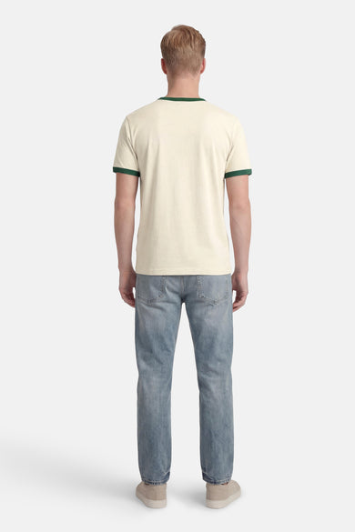 T-shirt beige à manches courtes de ORIGINALS BY JACK & JONES, avec des accents verts au col et aux manches, porté avec un jean et des baskets.