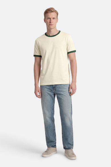 T-shirt beige à manches courtes de ORIGINALS BY JACK & JONES, avec une bordure verte au col et aux manches, porté avec un jean et des baskets.