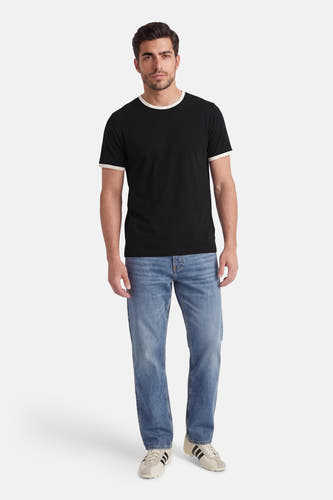 T-shirt noir à manches courtes de ORIGINALS BY JACK & JONES, avec des bords blancs, porté avec un jean bleu et des baskets de couleur crème.