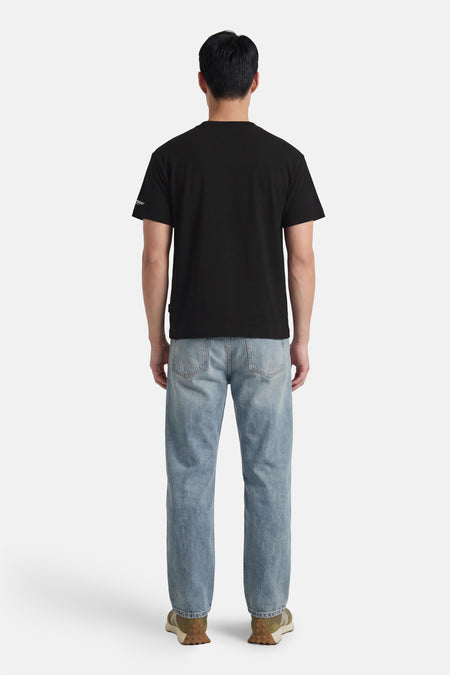 T-shirt noir à manches courtes de ORIGINALS BY JACK & JONES, sur un homme avec un jean clair et des baskets vert olive.