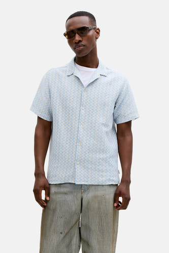 Chemise bleue à manches courtes de ORIGINALS BY JACK & JONES, avec un motif subtil, portée avec une veste beige et un t-shirt blanc.