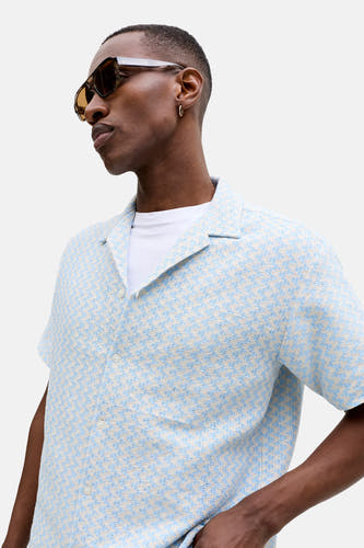 Chemise bleue à manches courtes de ORIGINALS BY JACK & JONES, avec un motif à carreaux bleu et blanc et portée sur un t-shirt blanc.