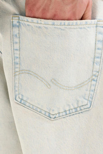 Short en jean bleu clair de JACK & JONES JEANS INTELLIGENCE avec une main dans la poche arrière et des surpiqûres jaunes.
