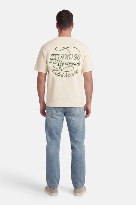 T-shirt écru à manches courtes de Originals by Jack & Jones, avec texte vert au dos et jean.