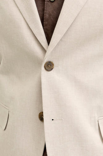 Détail d'un blazer écru de PREMIUM by JACK & JONES en tissu texturé, avec des boutons marron et une chemise marron en dessous.