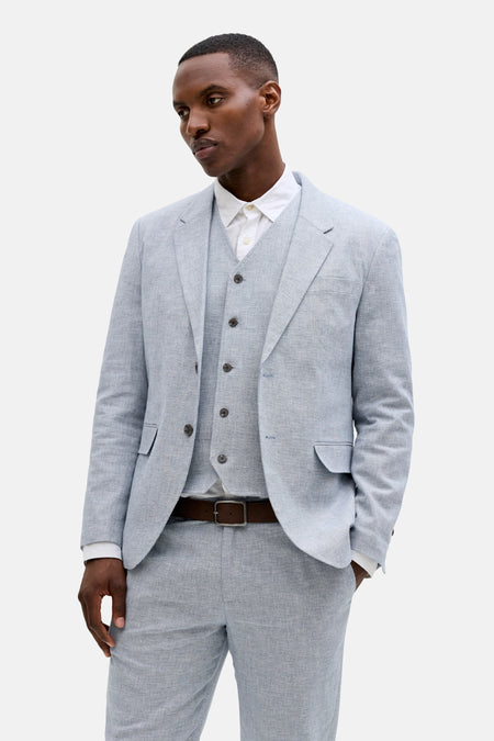 Blazer bleu clair de PREMIUM by JACK & JONES avec texture lin, porté avec un gilet et une chemise blanche.