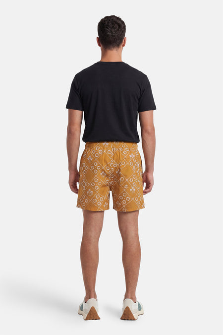 Gele zwemshort van PREMIUM by JACK & JONES met wit bloem- en ruitpatroon, van achteren gezien, gedragen met zwart T-shirt en sneakers.