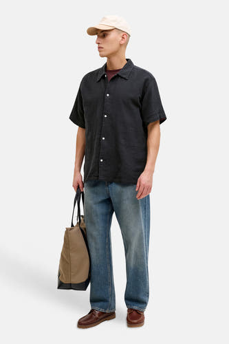 Chemise noire à manches courtes de ORIGINALS BY JACK & JONES, avec boutons blancs, portée avec un jean, des chaussures marron et une casquette beige.