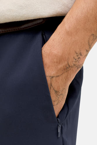 Pantalon de costume bleu de PREMIUM by JACK & JONES, avec ceinture marron et une main dans la poche.