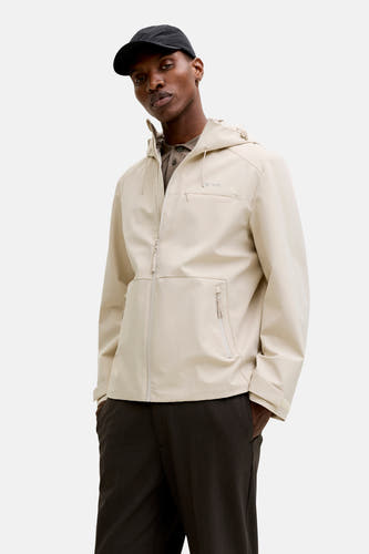 Veste courte écru de PREMIUM by JACK & JONES, avec capuche, portée sur un polo marron et un pantalon foncé.