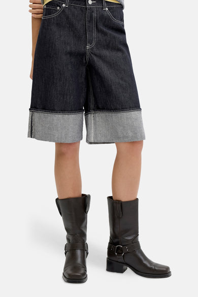 Short en jean bleu marine de JJXX, avec ourlet retroussé, combiné avec un polo gris rayé et des bottes marron.