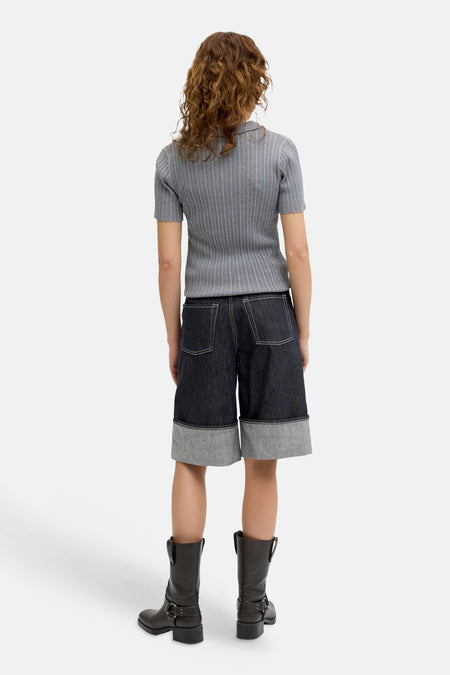 Short en jean bleu marine de JJXX, avec surpiqûres blanches et un large ourlet retroussé, porté avec des bottes en cuir marron.