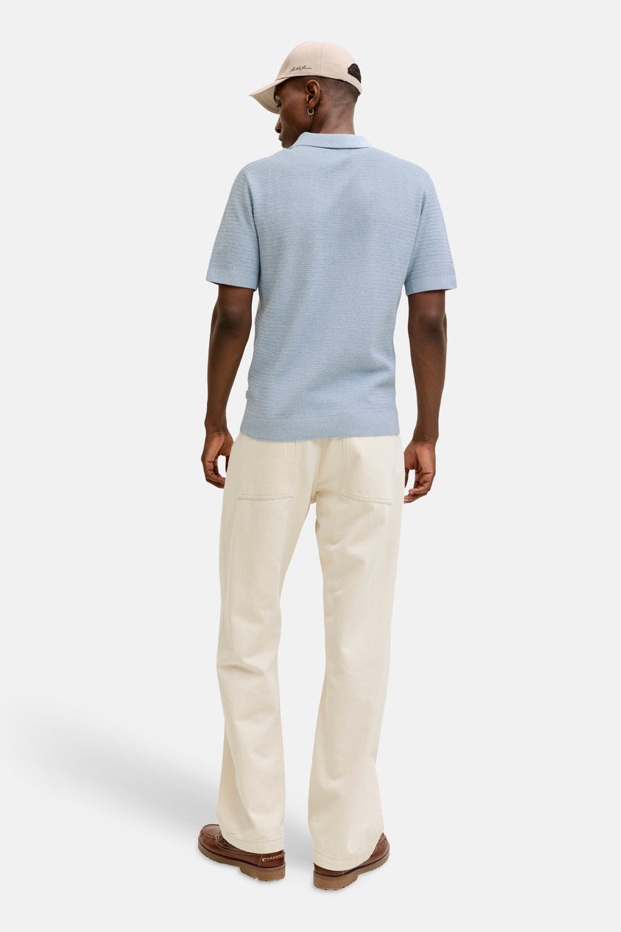 Polo bleu à manches courtes de PREMIUM BLUE by JACK & JONES, vue de dos, combinée avec un pantalon crème et une casquette.