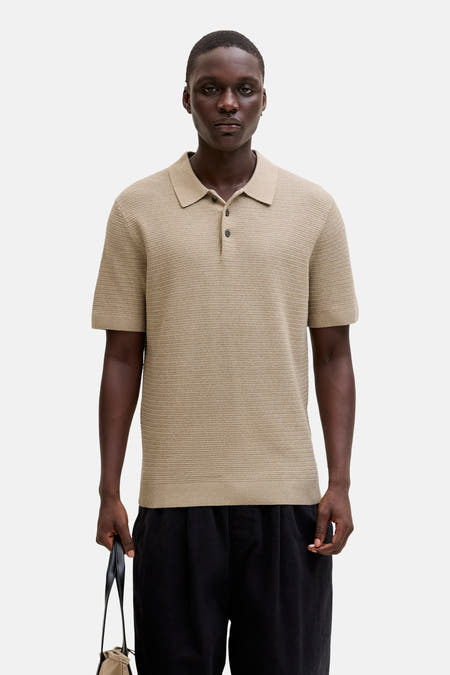 Polo beige à manches courtes de PREMIUM BLUE par JACK & JONES, avec un subtil motif texturé et porté avec un pantalon noir et une sacoche.