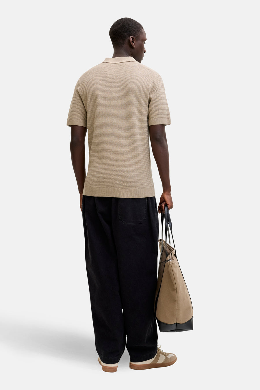 Beige polo met korte mouwen van PREMIUM BLUE by JACK & JONES, met subtiel textuurpatroon en gedragen met zwarte broek en tas.