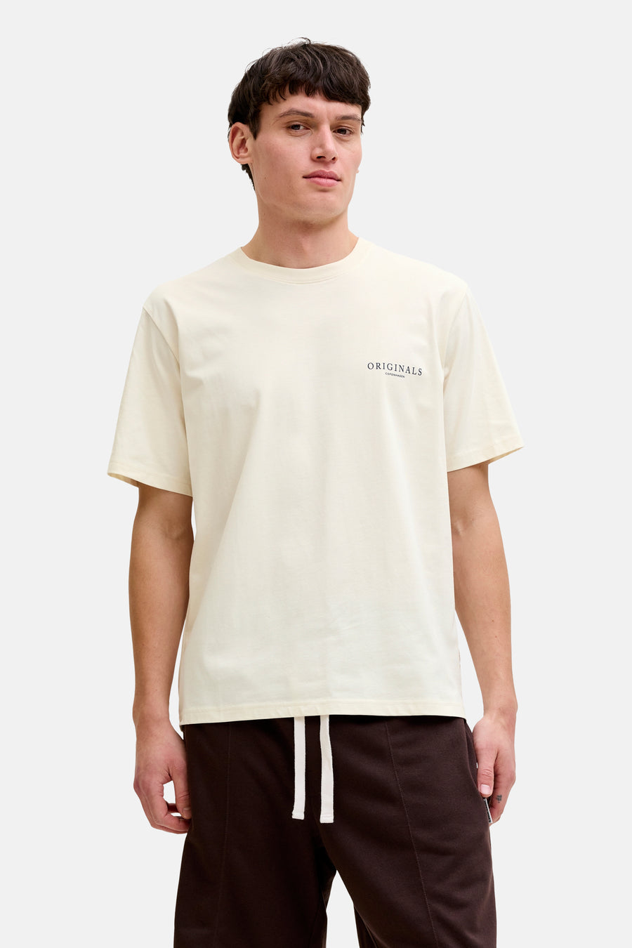 T-shirt écru de ORIGINALS BY JACK & JONES, à manches courtes, porté avec une veste beige, un short marron et des bottines à lacets jaunes.