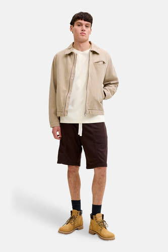 Ecru T-shirt van ORIGINALS BY JACK & JONES, met korte mouwen, gedragen met een beige jas, bruine shorts en gele veterlaarzen.
