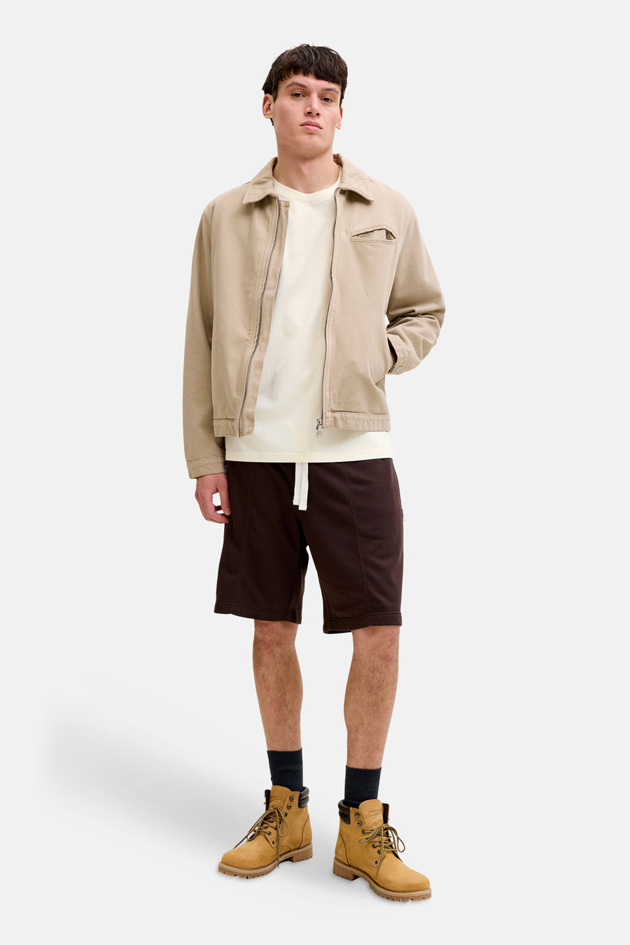Ecru T-shirt van ORIGINALS BY JACK & JONES, met korte mouwen, gedragen met een beige jas, bruine shorts en gele veterlaarzen.
