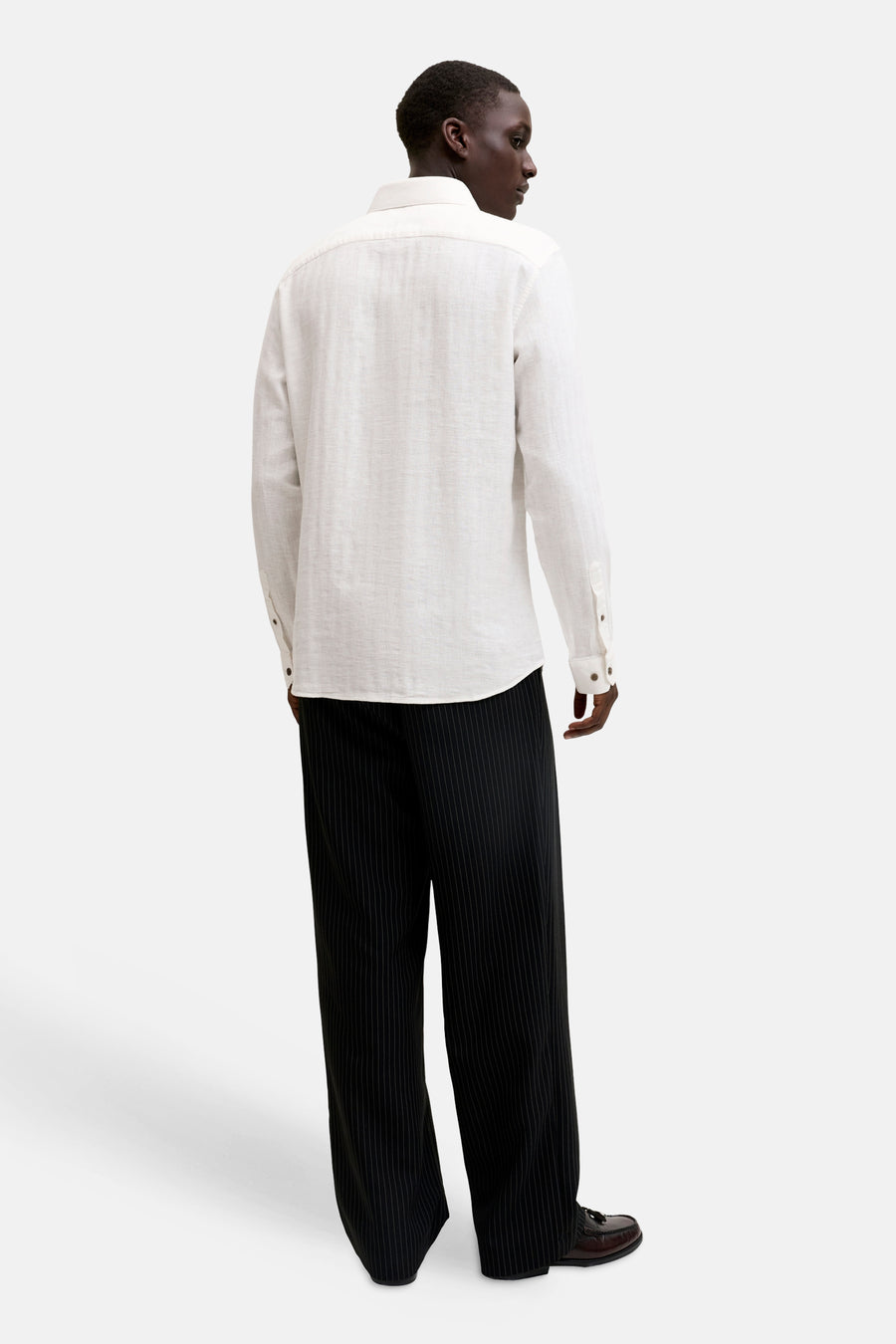 Chemise blanche structurée à manches longues de PREMIUM by JACK & JONES, vue de dos, portée avec un pantalon noir à fines rayures et des mocassins marron foncé.