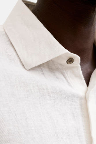 Chemise blanche de PREMIUM by JACK & JONES avec une texture tissée, un fin chevrons sur le col et un bouton foncé, portée sur une peau foncée.