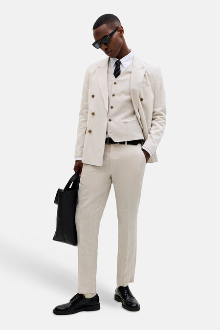 Ecru gilet van PREMIUM by JACK & JONES, gedragen over een wit overhemd met gestreepte das, onder een beige pak met tas.
