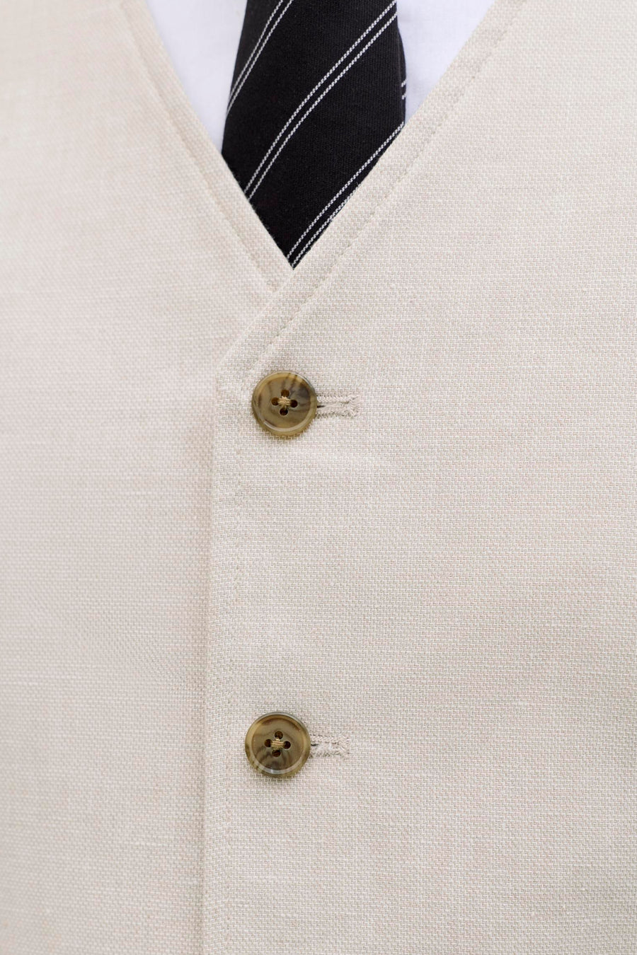 Gilet écru de PREMIUM by JACK & JONES, avec deux boutons, porté sur une chemise blanche avec une cravate noire rayée.