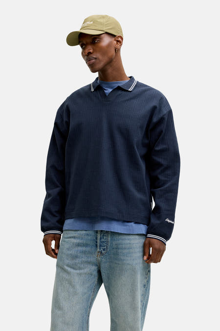 Pull bleu à col rond de ORIGINALS BY JACK & JONES, porté avec une veste en cuir, un jean et une casquette.