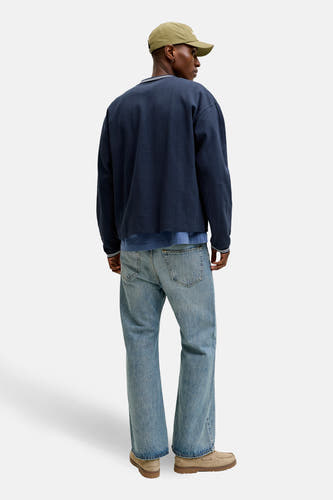 Pull bleu de ORIGINALS BY JACK & JONES, avec un motif subtilement rayé, combiné avec un jean et une casquette kaki.