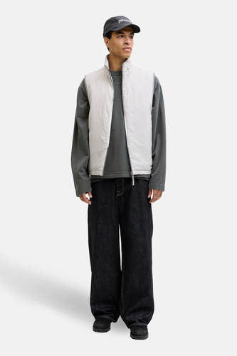 Pull noir à col rond de CORE BY JACK & JONES, combiné avec un gilet sans manches blanc, un jean ample et une casquette.