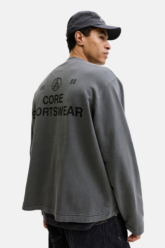 Pull noir à col rond de CORE BY JACK & JONES, avec imprimé au dos, porté avec une casquette foncée.
