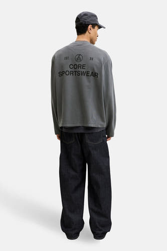 Pull noir à col rond de CORE BY JACK & JONES, avec logo dans le dos, porté avec une casquette et un jean ample.