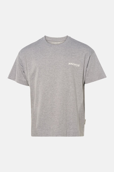 T-shirt gris à manches courtes de CORE BY JACK & JONES, porté avec un jean bleu troué et des baskets beiges.