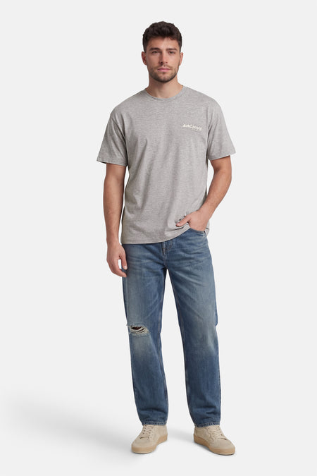 Grijs T-shirt met korte mouwen van CORE BY JACK & JONES, gedragen met blauwe jeans met een gat en beige sneakers.