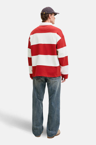 Pull rouge à col rond de ORIGINALS BY JACK & JONES, avec des rayures blanches horizontales et porté avec un jean et une casquette.